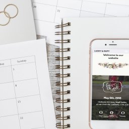 Wedding website on phone, placed on top of notebook with wedding rings