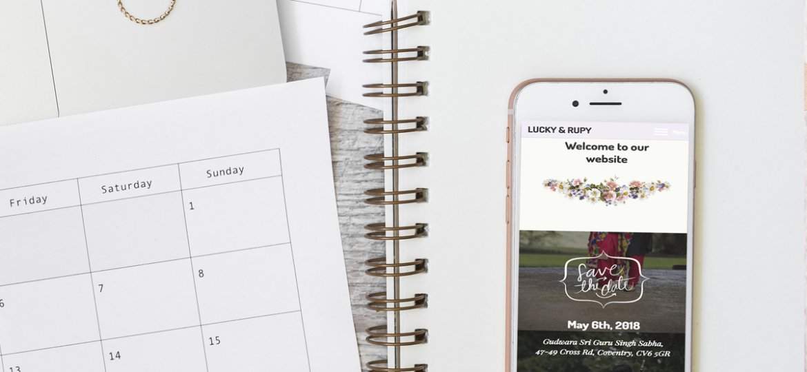 Wedding website on phone, placed on top of notebook with wedding rings